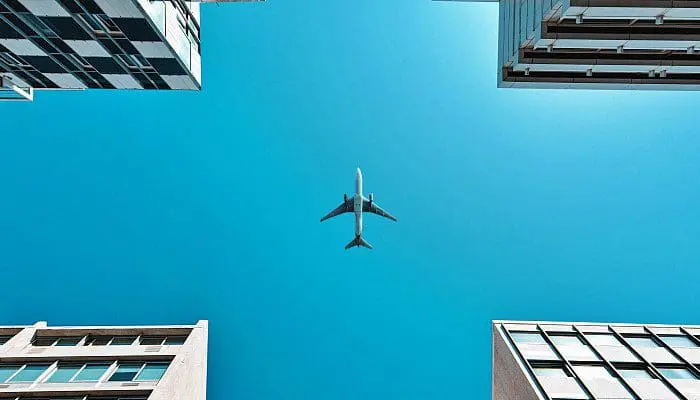 Avião visto entre prédios (foto: Marios Gkortsilas - Unsplash)