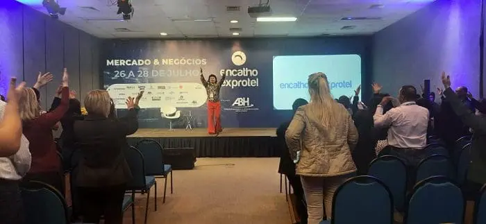 Xuxu faz coreografia com participantes na abertura das capacitações do Encatho & Exprotel 2022. A maioria está com braços levantados, comemorando, no Encatho & Exprotel 2022, em Florianópolis-SC.