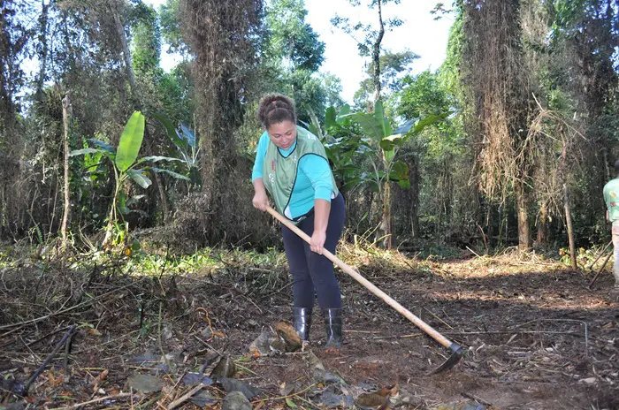 Uma monitora ambiental, com uma enxada na mão, carpindo um pequeno espaço da área