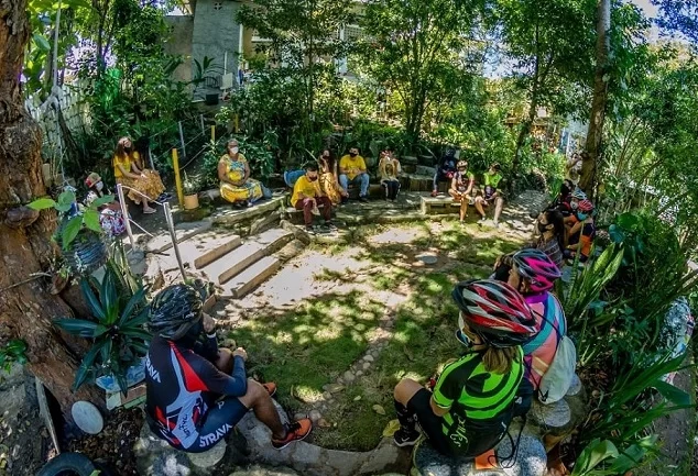 Pessoas em roda, com trajes de ciclista, em uma região com vegetação e árvores em João Pessoa. O Cicloturismo é um dos tipos de turismo de base comunitária em João Pessoa, e João Pessoa firma Termo de Compromisso para desenvolvimento do setor de turismo comunitário.