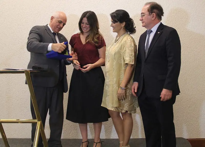 Dilson Jatahy (presidente da ABIH) oficializa a parceria entregando uma placa a Camila observados por Vanessa Moraes (presidente da ABIH-GO) e Manoel Linhares (presidente eleito para o biênio 2018-2019)