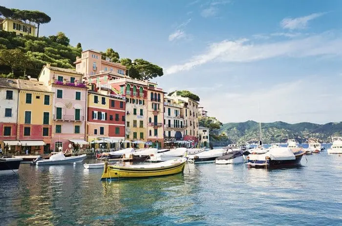 A aldeia de Portofino, localizada a sudeste de Gênova, na Itália, com construções coloridas à beira-mar e vários barcos pequenos.