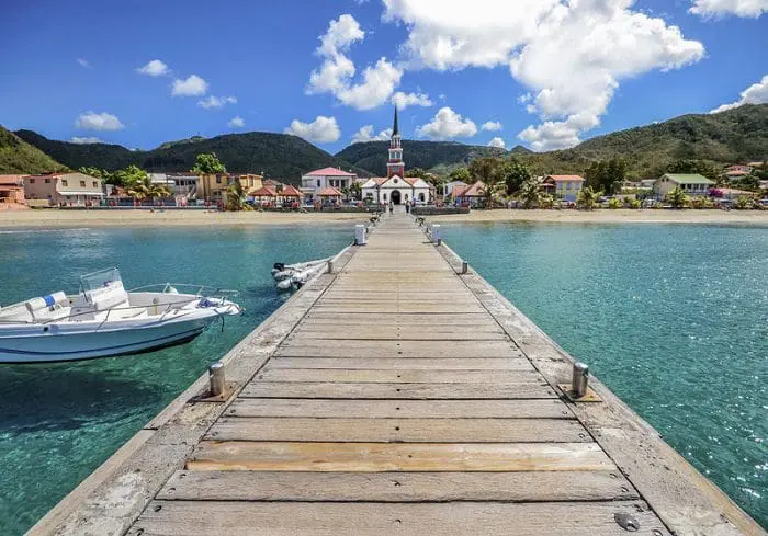 O porto de Fort-de-France, em Martinica, com águas azuis cristalinas e visão para a praia, que possui algumas construções.