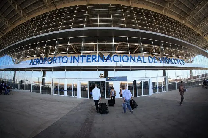 Fachada do Aeroporto Internacional de Viracopos, em Campinas-SP. Há alguns passageiros com malas entrando no aeroporto.