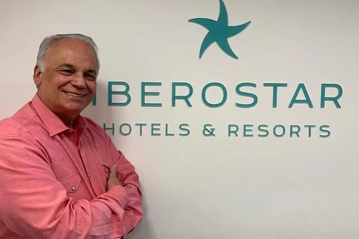 Orlando Giglio, de braços cruzados e camisa social rosa, em frente ao banner da Iberostar Hotels e Resorts. A rede hoteleira anunciou a saída do executivo.