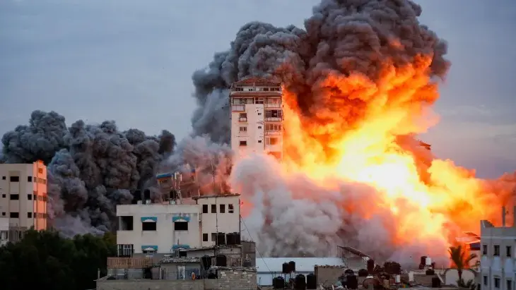 Artigo conflito na faixa de Gaza e a Paz mundial: foto de prédio na faixa de Gaza, soltando fumaça e fogo, após ser bombardeado por Israel