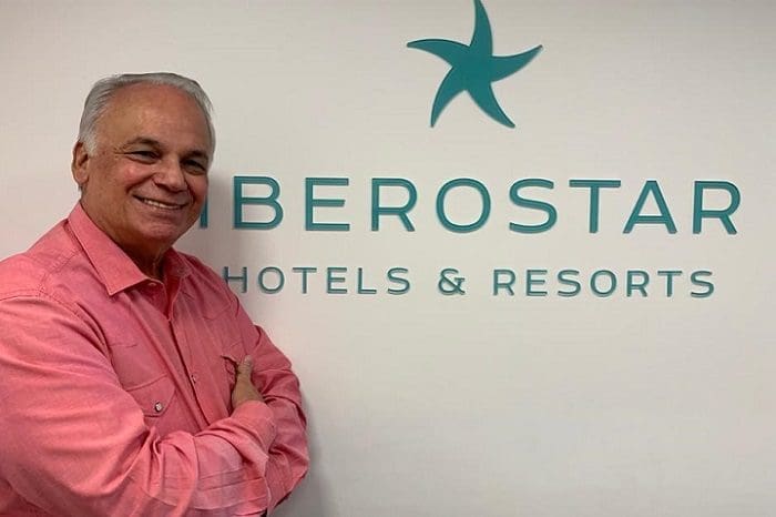 Orlando Giglio, de braços cruzados e camisa social rosa, em frente ao banner da Iberostar Hotels e Resorts. A rede hoteleira anunciou a saída do executivo.