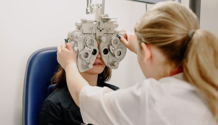 GTA encabeça luta conta o estrabismo: foto de uma médica, examinando os olhos de uma paciente, segurando um aparelho na frente dos olhos dela, para examinar a paciente